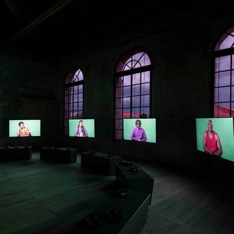 Medieninstallation mit synchronisierten Videodisplays Raum mit mehreren Bildschirmen, die Personen vor grünem Hintergrund zeigen.